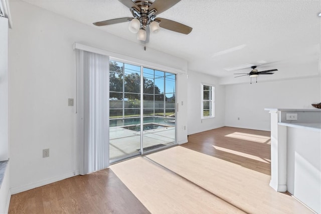 interior space featuring ceiling fan, a textured ceiling, baseboards, and wood finished floors