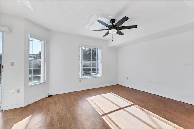 spare room with a wealth of natural light, a textured ceiling, baseboards, and wood finished floors