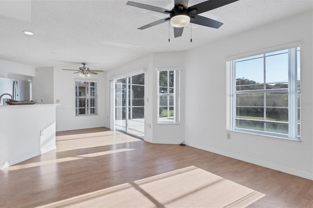 unfurnished living room featuring a textured ceiling, baseboards, and wood finished floors