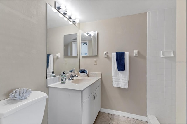 full bathroom with toilet, vanity, tile patterned flooring, tiled shower, and baseboards