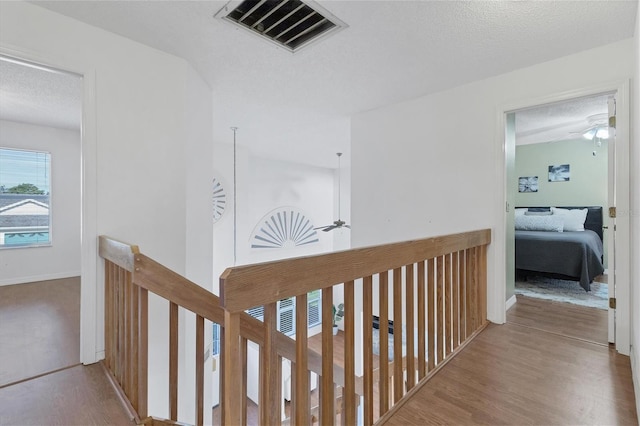 hallway featuring a textured ceiling, wood finished floors, an upstairs landing, visible vents, and baseboards