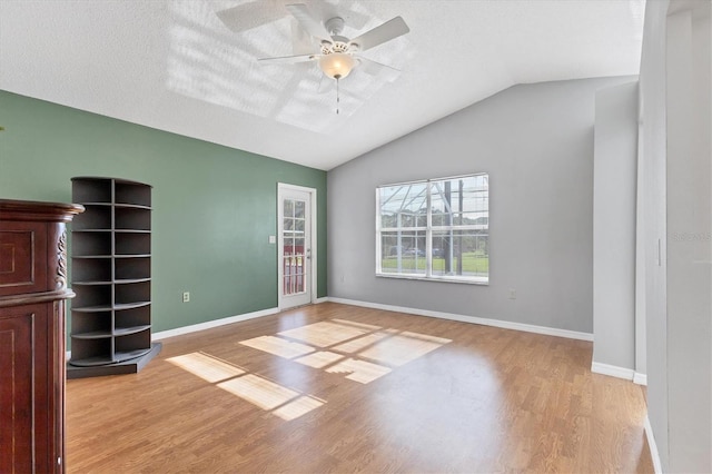 unfurnished living room with vaulted ceiling, wood finished floors, a ceiling fan, and baseboards