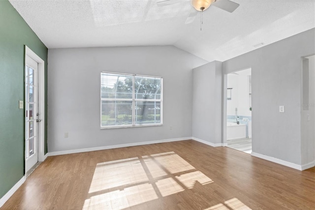 spare room featuring vaulted ceiling, a textured ceiling, wood finished floors, and baseboards