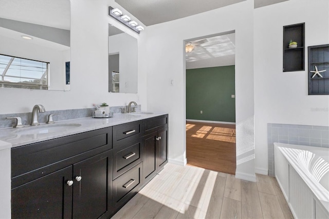 bathroom with double vanity, a sink, a bathing tub, and wood finished floors