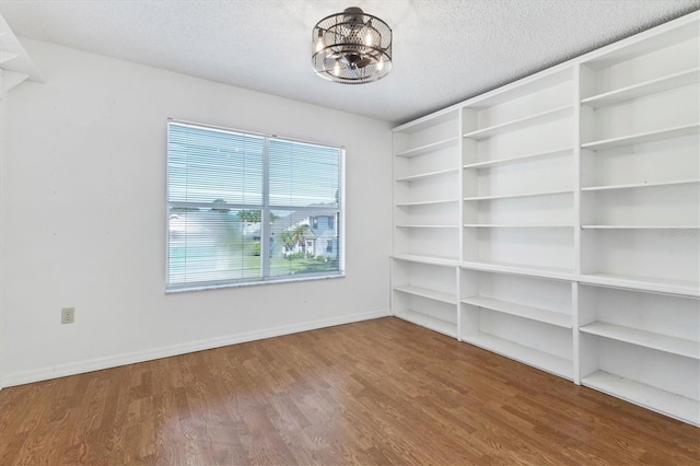 empty room with baseboards, a textured ceiling, an inviting chandelier, and wood finished floors