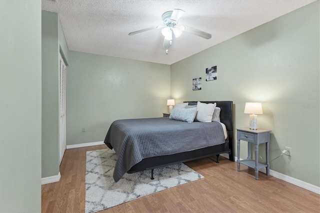 bedroom featuring ceiling fan, a textured ceiling, baseboards, and wood finished floors