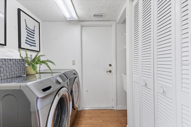 clothes washing area with laundry area, wood finished floors, visible vents, and washer and dryer