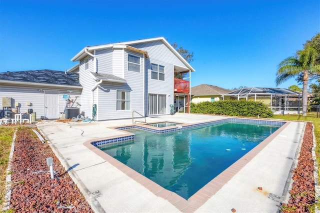 rear view of house with a patio, a balcony, an in ground hot tub, central AC, and an outdoor pool