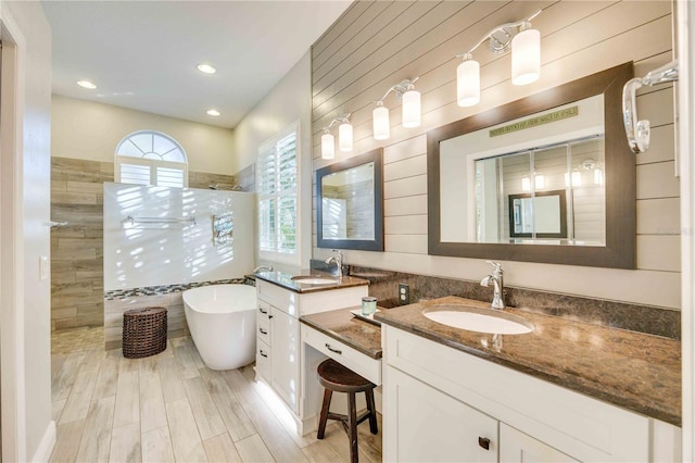 full bath featuring a freestanding bath, two vanities, walk in shower, and a sink