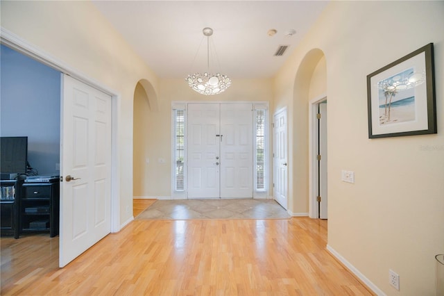 entrance foyer featuring visible vents, arched walkways, baseboards, and light wood-style flooring