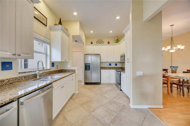 kitchen with light stone countertops, a notable chandelier, white cabinets, stainless steel appliances, and a sink