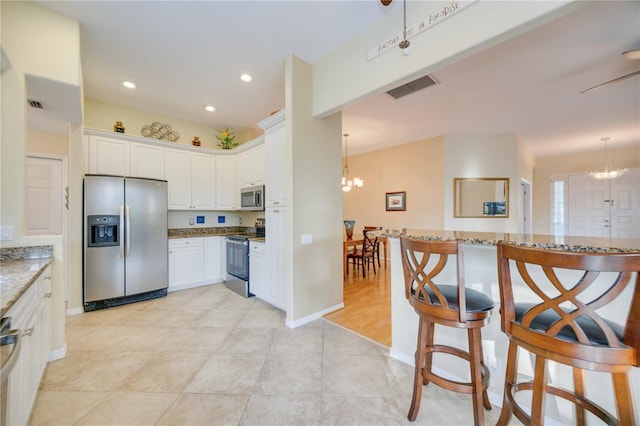 kitchen with light stone counters, visible vents, stainless steel appliances, white cabinets, and a notable chandelier