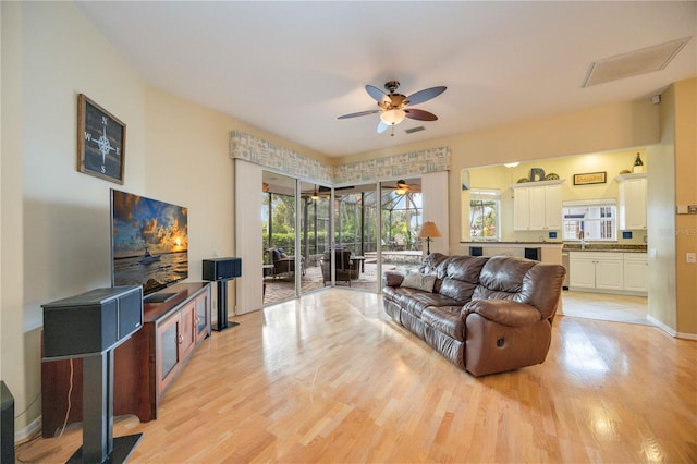 living area with baseboards, ceiling fan, and light wood finished floors