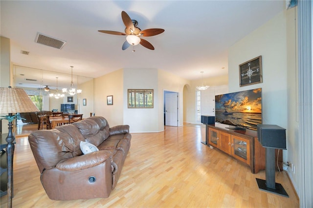 living room featuring ceiling fan with notable chandelier, arched walkways, visible vents, and light wood finished floors