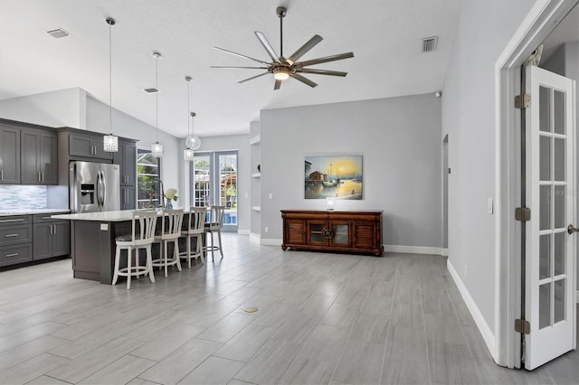 kitchen with a breakfast bar, a center island, hanging light fixtures, vaulted ceiling, and stainless steel fridge with ice dispenser