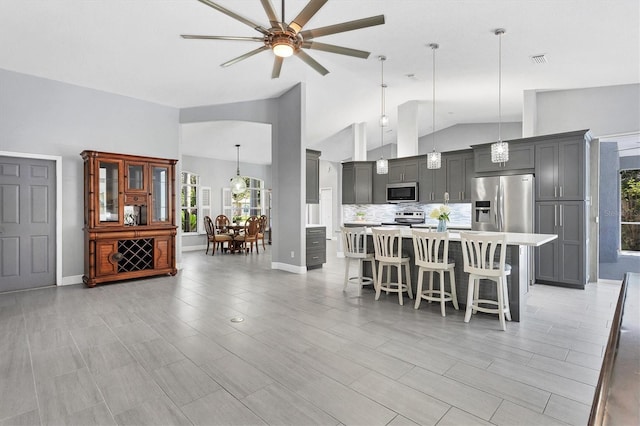 kitchen with stainless steel appliances, high vaulted ceiling, a wealth of natural light, and a breakfast bar area