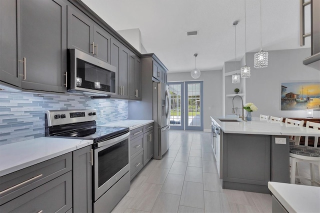 kitchen with sink, hanging light fixtures, stainless steel appliances, decorative backsplash, and a kitchen island with sink