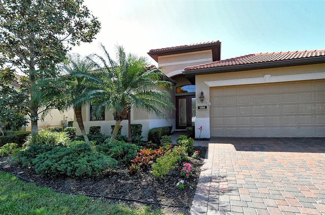 mediterranean / spanish-style house with a garage, decorative driveway, a tiled roof, and stucco siding