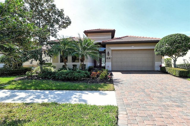 mediterranean / spanish house featuring an attached garage, a tile roof, decorative driveway, and stucco siding