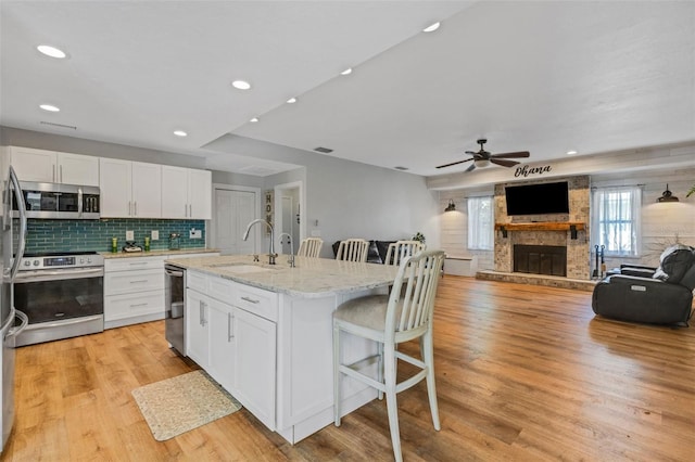 kitchen with a fireplace, appliances with stainless steel finishes, light stone counters, sink, and an island with sink