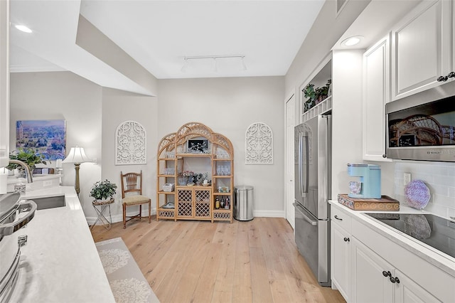 kitchen featuring light wood-type flooring, track lighting, tasteful backsplash, white cabinetry, and appliances with stainless steel finishes