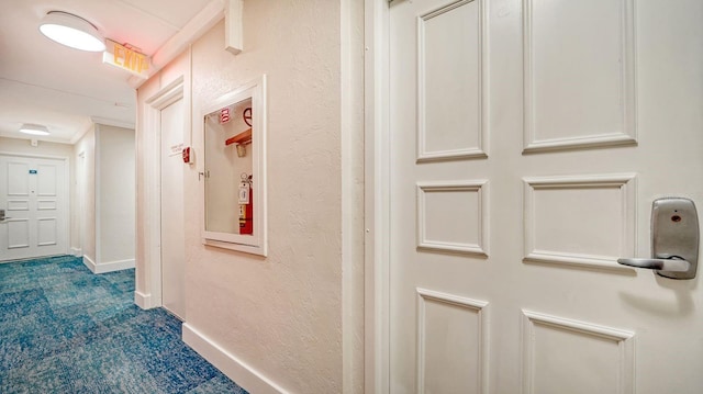 hall with baseboards, dark carpet, and a textured wall