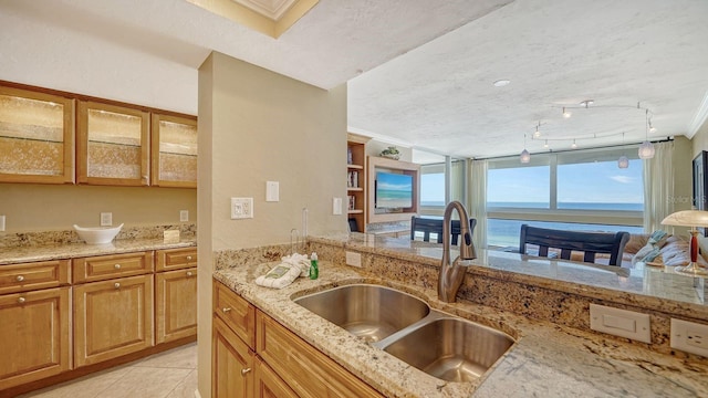 kitchen with light stone counters, a textured ceiling, crown molding, a sink, and light tile patterned flooring