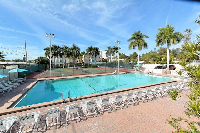 pool with a tennis court, fence, and a patio