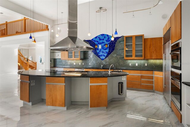 kitchen with hanging light fixtures, a kitchen island with sink, stainless steel oven, island range hood, and tasteful backsplash