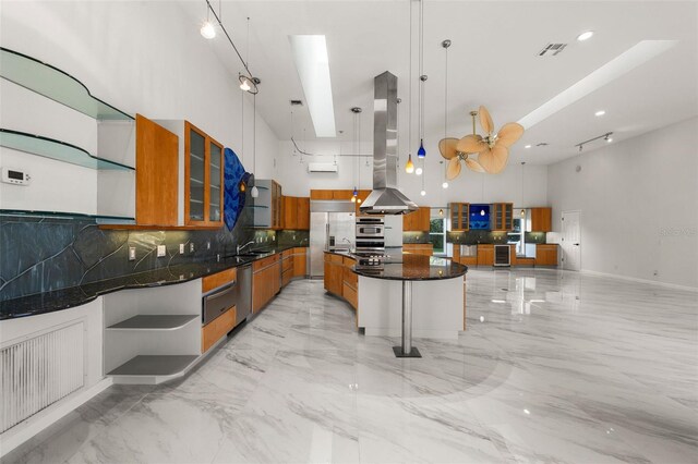 kitchen with dark stone countertops, island range hood, a center island, decorative backsplash, and hanging light fixtures