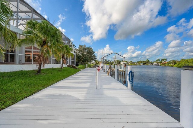 dock area featuring glass enclosure, a water view, and a lawn