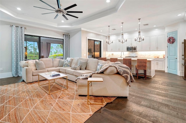 living room with hardwood / wood-style floors, ceiling fan with notable chandelier, a raised ceiling, and ornamental molding