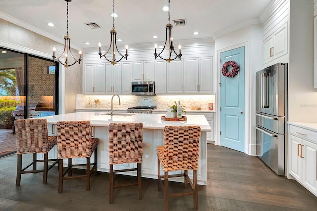 kitchen with an inviting chandelier, appliances with stainless steel finishes, dark wood-type flooring, pendant lighting, and a center island with sink