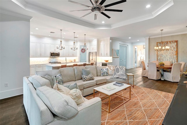 living room featuring ceiling fan with notable chandelier, ornamental molding, wood-type flooring, sink, and a raised ceiling