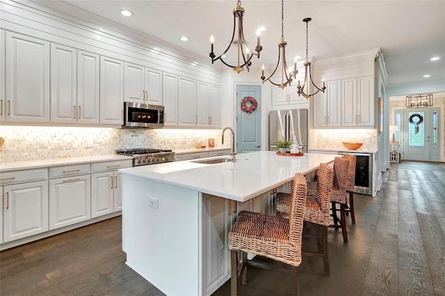 kitchen with a kitchen island with sink, a notable chandelier, stainless steel appliances, sink, and dark hardwood / wood-style floors