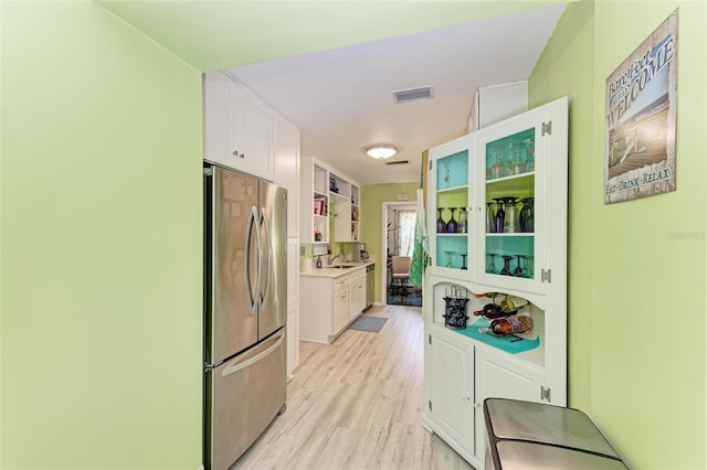 kitchen featuring visible vents, white cabinets, freestanding refrigerator, light countertops, and light wood-type flooring