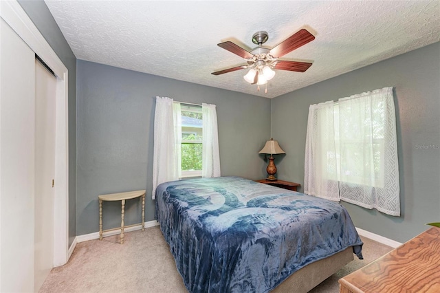 carpeted bedroom with a textured ceiling, a closet, a ceiling fan, and baseboards