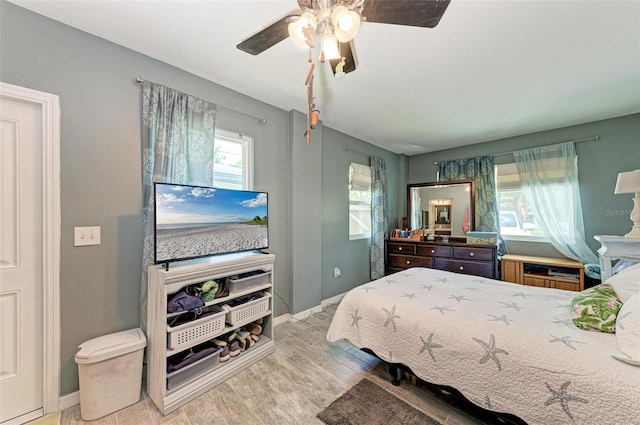 bedroom featuring ceiling fan, multiple windows, baseboards, and wood finished floors