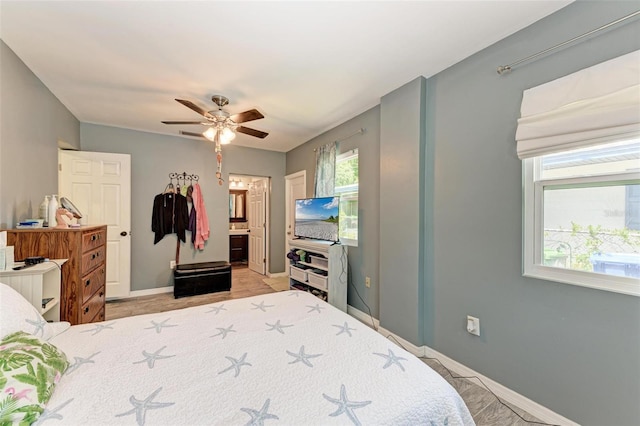 bedroom with ceiling fan, ensuite bath, and baseboards