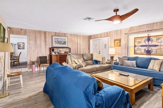 living room featuring ceiling fan, wood walls, and light hardwood / wood-style floors