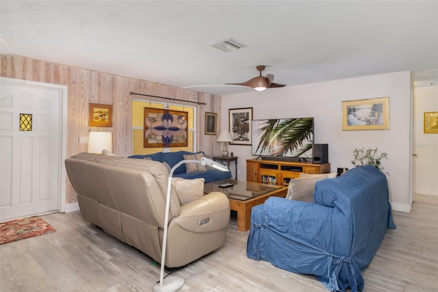 living room with wooden walls, ceiling fan, and light hardwood / wood-style floors