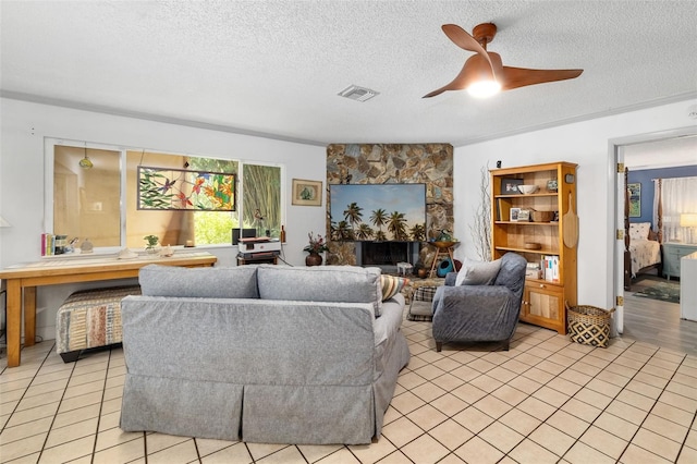 living room featuring a textured ceiling, light tile patterned floors, ceiling fan, and a stone fireplace