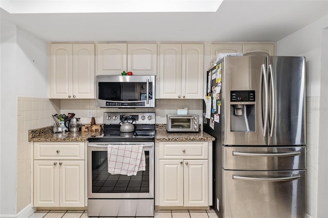 kitchen featuring light tile patterned floors, appliances with stainless steel finishes, dark stone countertops, and decorative backsplash