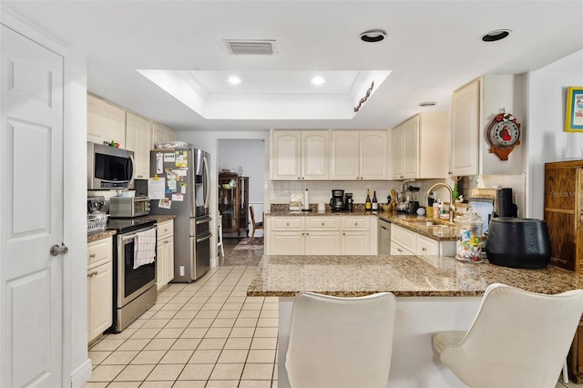 kitchen with appliances with stainless steel finishes, decorative backsplash, a raised ceiling, and kitchen peninsula