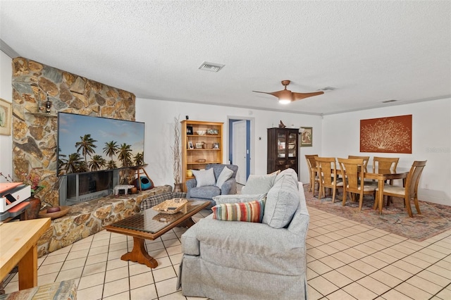 tiled living room featuring a textured ceiling, ceiling fan, and a fireplace