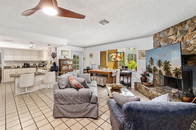 tiled living room featuring a stone fireplace, ceiling fan, and a textured ceiling