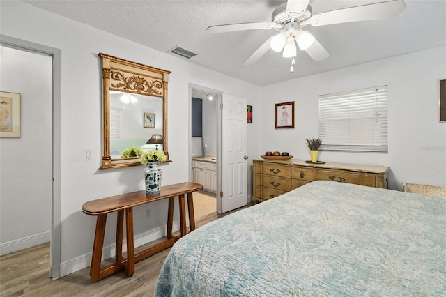 bedroom featuring ensuite bath, a textured ceiling, light hardwood / wood-style flooring, and ceiling fan