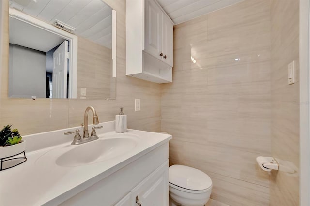 bathroom featuring vanity, toilet, and tile walls