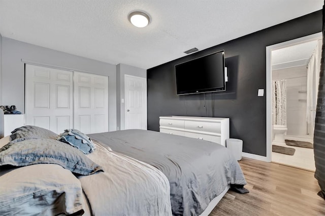 bedroom with ensuite bath, a closet, a textured ceiling, and light hardwood / wood-style floors