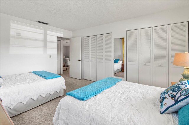 carpeted bedroom with visible vents, a textured ceiling, and multiple closets